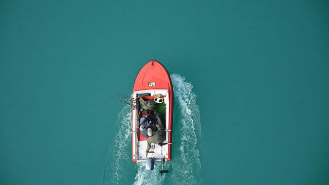 Top view of a red motorboat with fishermen navigating open turquoise waters.